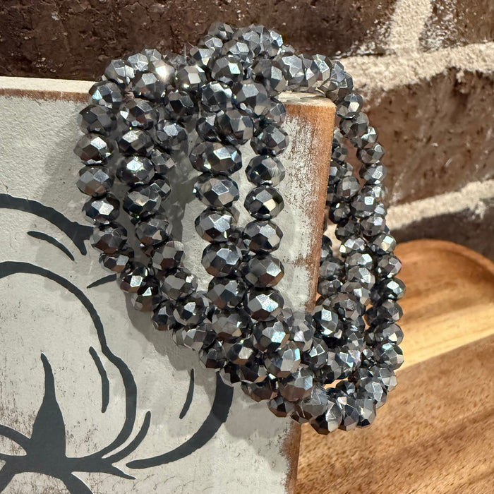 Black beaded bracelet on a wooden surface with a stone wall background