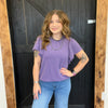 Woman wearing a purple top and blue jeans standing in front of a wooden door.