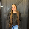 Young woman with long hair wearing a black top and blue jeans standing in front of a wooden door.