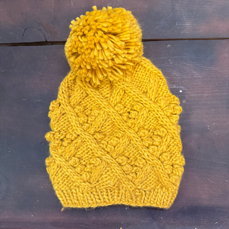 Yellow knitted beanie with a pom-pom on a dark wooden surface