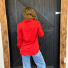 Person wearing a red jacket and blue jeans opening a wooden door.