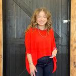 Woman wearing a bright red sweater standing in front of a wooden door.