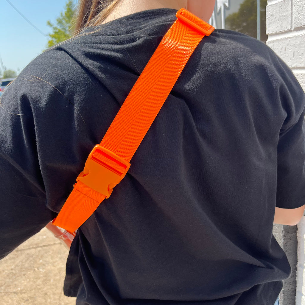 Person wearing a black shirt with an orange strap over shoulder outdoors