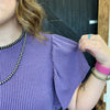 Person wearing a purple textured top with visible jewelry.