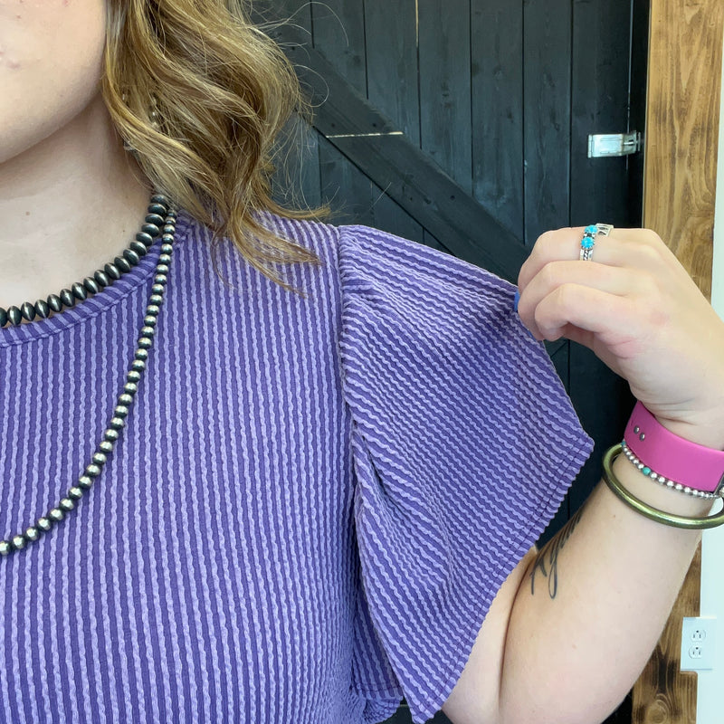 Person wearing a purple textured top with visible jewelry.