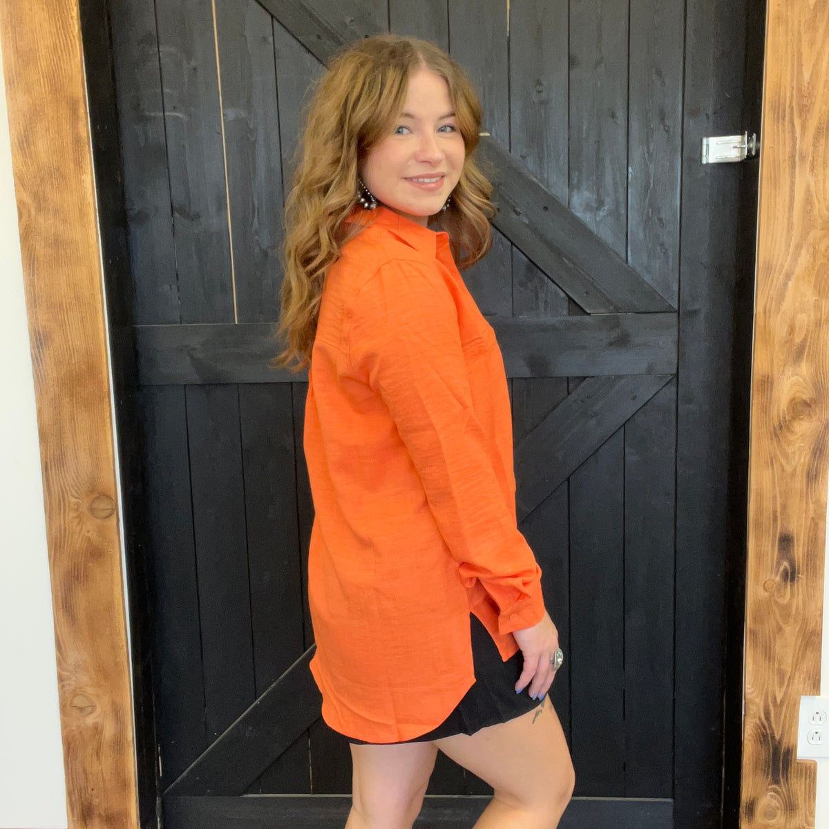 Woman wearing an orange jacket standing in front of a wooden door.