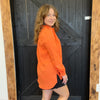 Woman wearing an orange jacket standing in front of a wooden door.