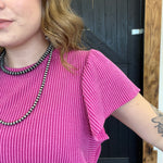 Person wearing a pink top and black and white necklace, standing in front of a wooden door.