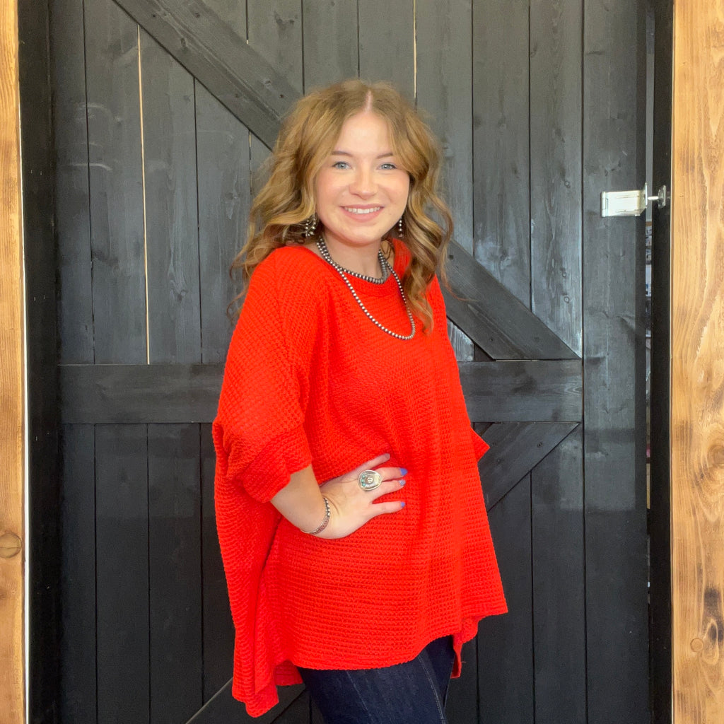Woman wearing a red sweater standing in front of a wooden door.
