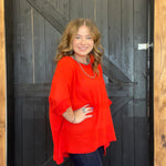Woman wearing a red sweater standing in front of a wooden door.