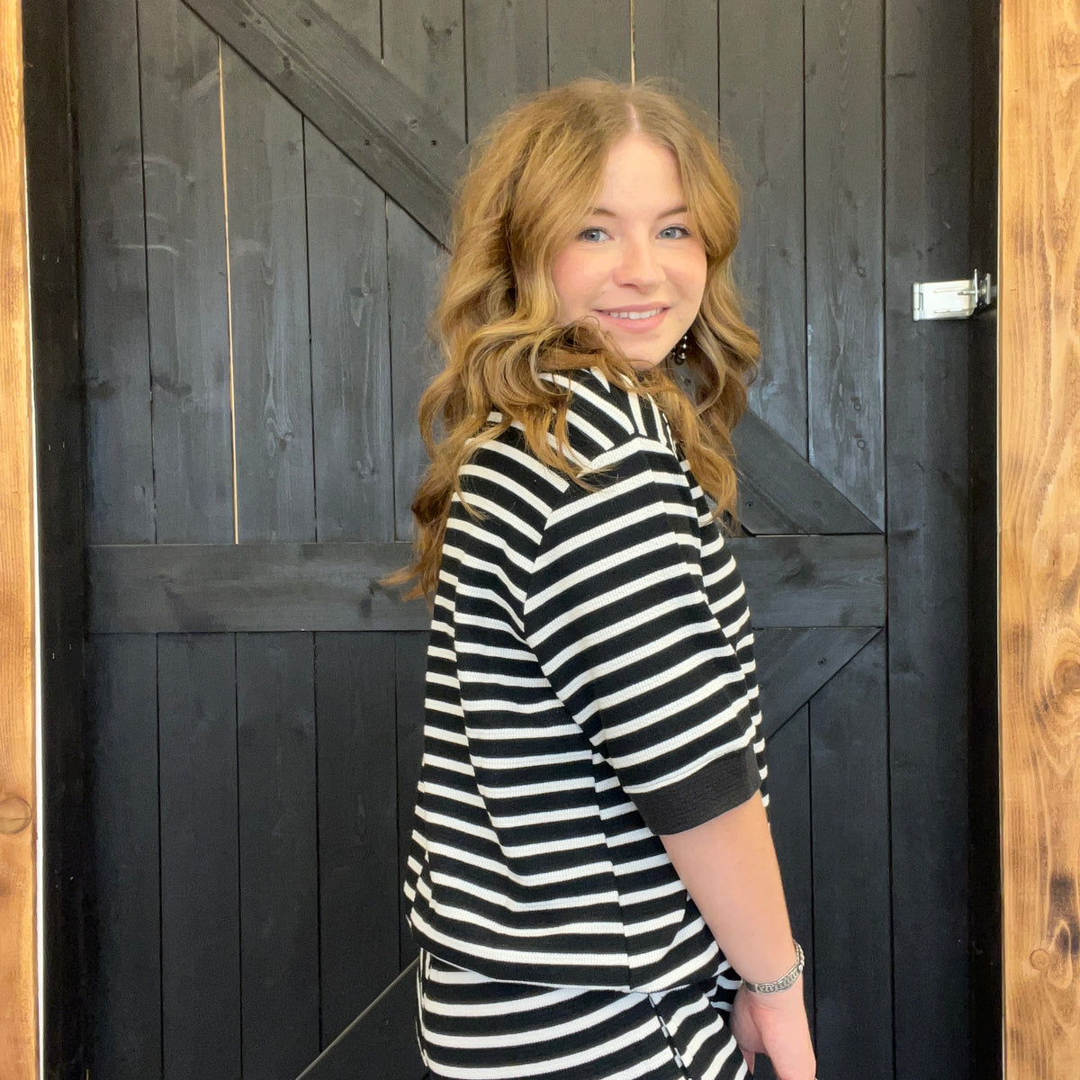 Woman wearing a black and white striped shirt standing in front of a wooden door.