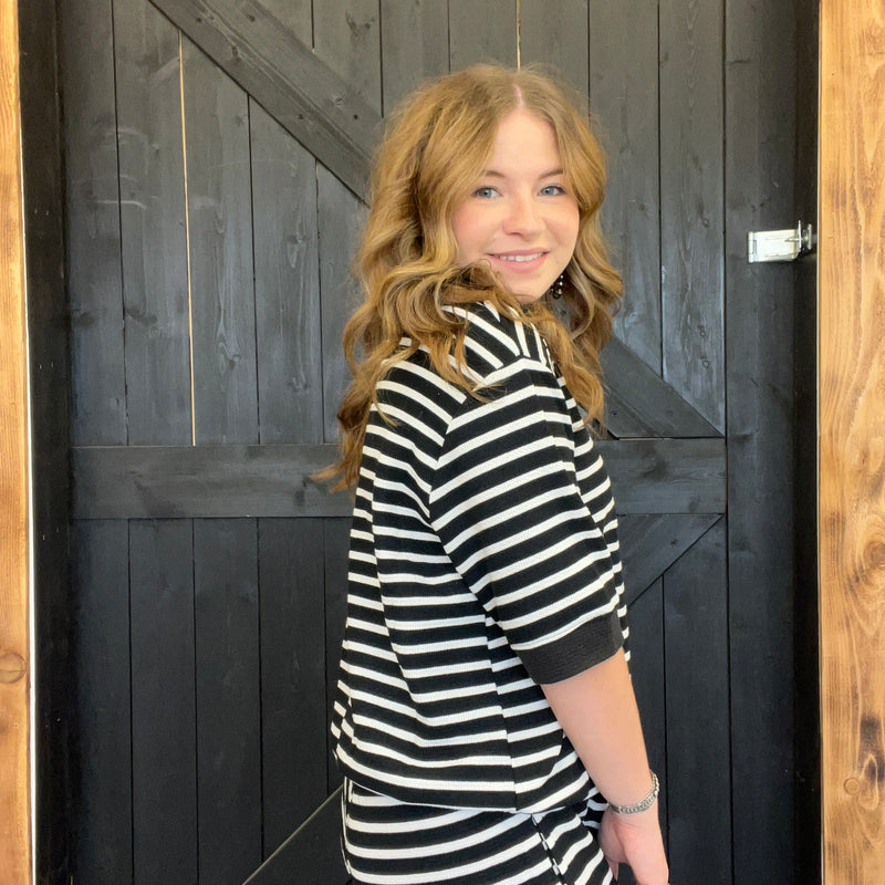 Woman wearing a black and white striped shirt standing in front of a wooden door.