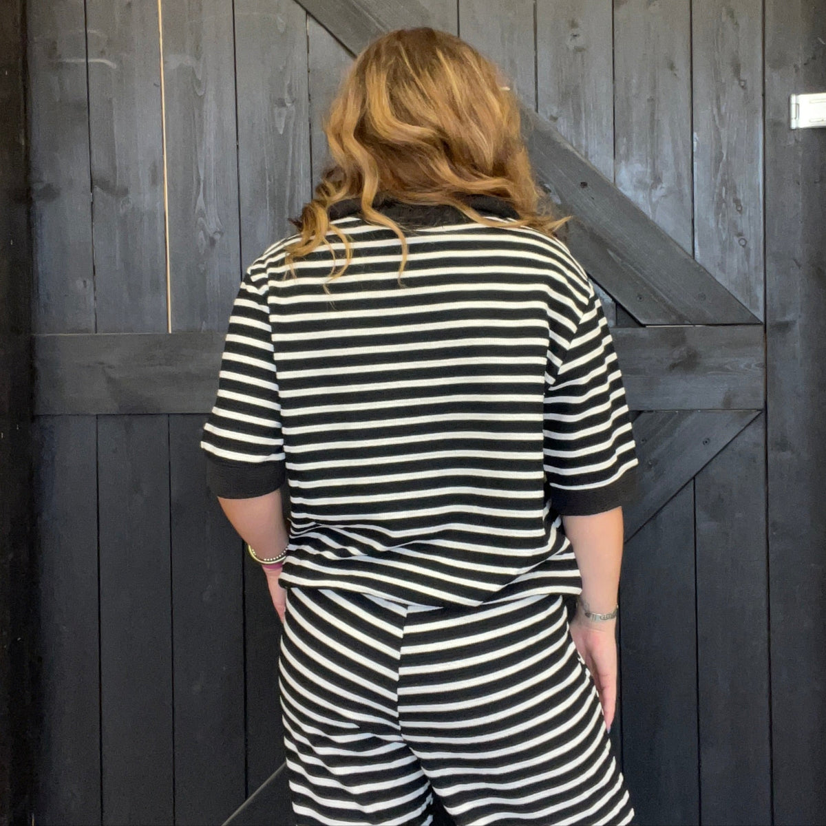 Person wearing a black and white striped outfit standing in front of a wooden door.
