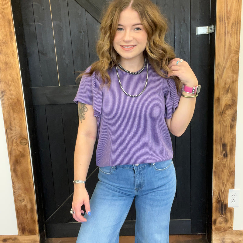 Person wearing a purple top and blue jeans standing in front of a wooden door.