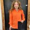 Woman wearing an orange shirt standing in front of a wooden door.
