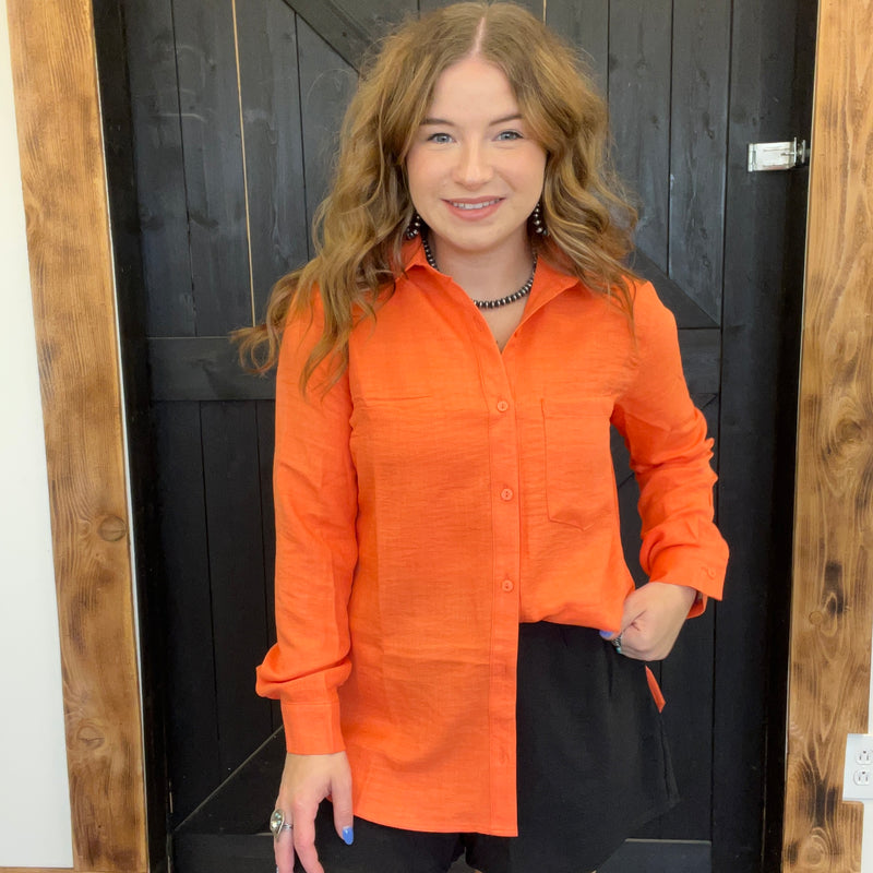Woman wearing an orange shirt standing in front of a wooden door.