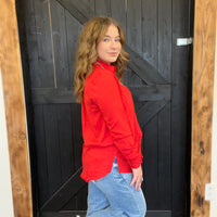 Woman in a red jacket and blue jeans standing in front of a black wooden door.
