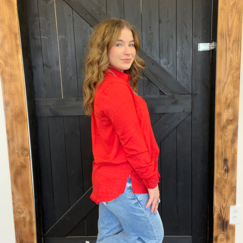 Woman in a red jacket and blue jeans standing in front of a black wooden door.
