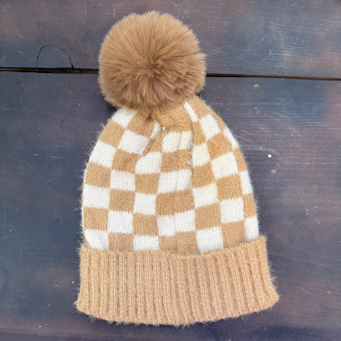 Knitted beanie with checkered pattern and brown pom-pom on a dark surface