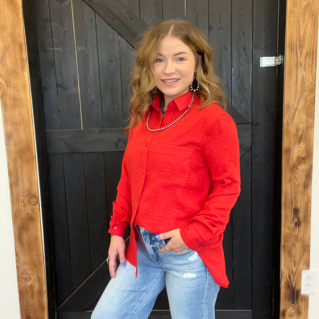 Woman wearing a red shirt and blue jeans standing in front of a wooden door.