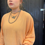 Person wearing a mustard yellow ribbed sweater with layered necklaces against a dark background