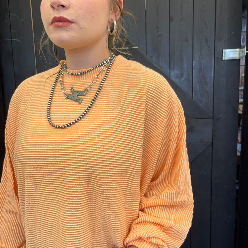 Person wearing a mustard yellow ribbed sweater with layered necklaces against a dark background