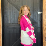Woman wearing a pink and white checkered sweater standing in front of a wooden door.