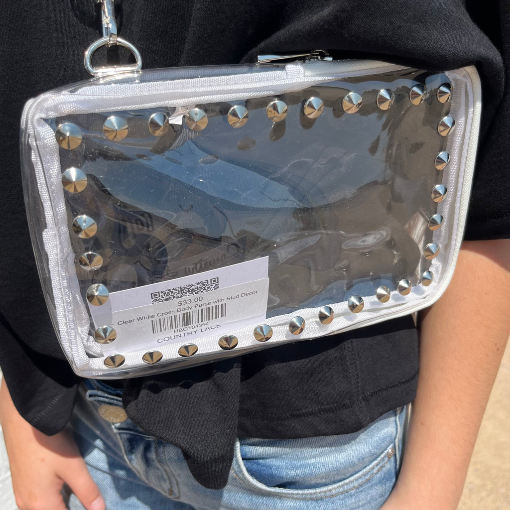 Clear handbag with silver studs held by a person wearing a black jacket and blue jeans.