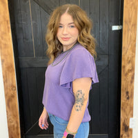 Woman wearing a purple top and blue jeans standing in front of a wooden door.