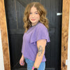 Woman wearing a purple top and blue jeans standing in front of a wooden door.