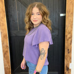 Woman wearing a purple top and blue jeans standing in front of a wooden door.