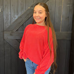 Young girl in a red sweater standing in front of a wooden door