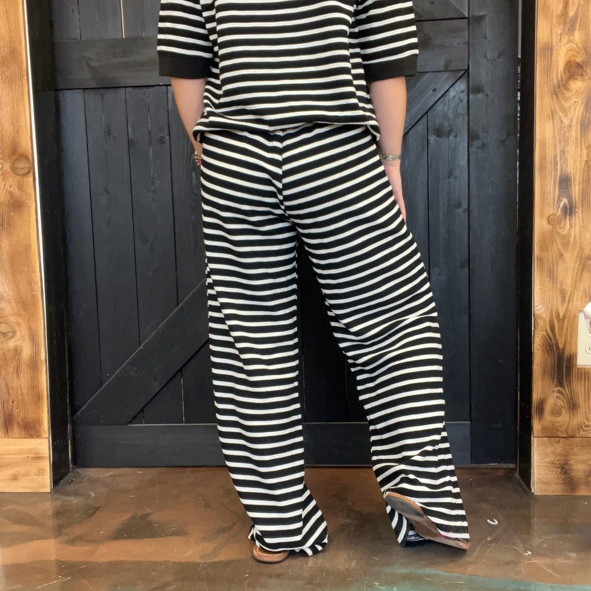 Person wearing a black and white striped outfit standing against a wooden door.