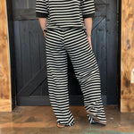 Person wearing a black and white striped outfit standing against a wooden door.