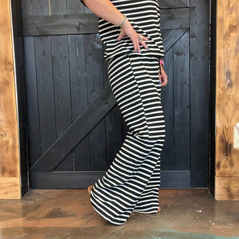 Person wearing black and white striped pants standing in front of a wooden door.