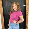 Woman wearing a pink top and blue jeans standing in front of a wooden door.