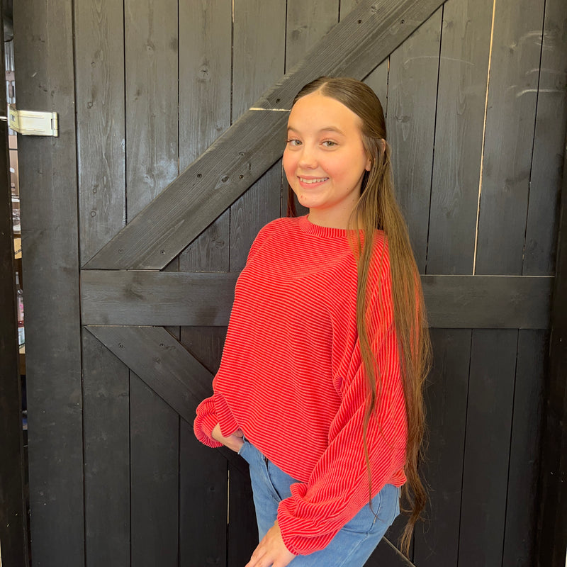 Young girl in a red sweater standing in front of a wooden door
