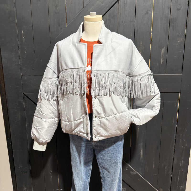 Mannequin wearing a light gray puffer jacket with fringe details against a dark wooden background.