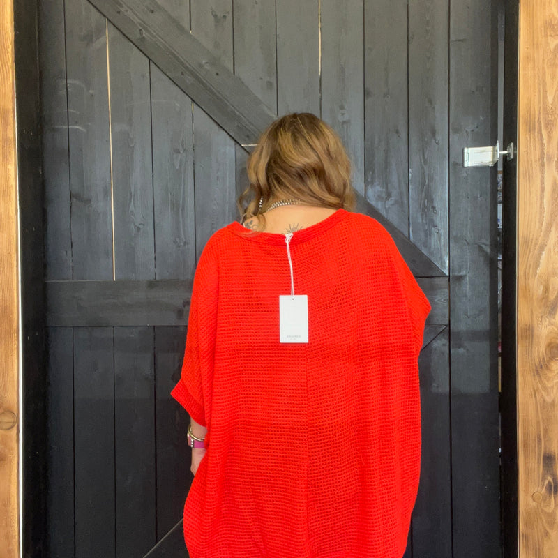 Person wearing a red garment with a tag, standing in front of a wooden door.