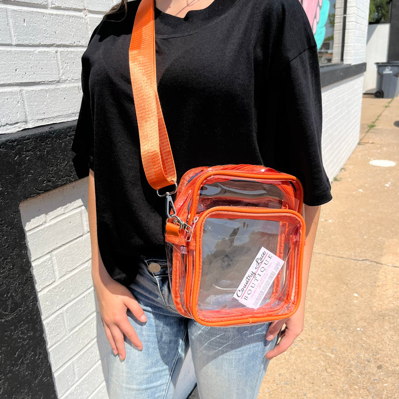 Person wearing a clear bag with an orange strap against a gray wall.