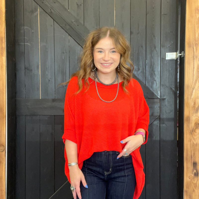 Woman wearing a red sweater and dark jeans standing in front of a wooden door.