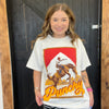 Woman wearing a white t-shirt with a graphic design and text, standing in front of a wooden door.