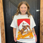 Woman wearing a white t-shirt with a graphic design and text, standing in front of a wooden door.