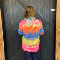 colorful sequin shirt standing in front of a wooden door.