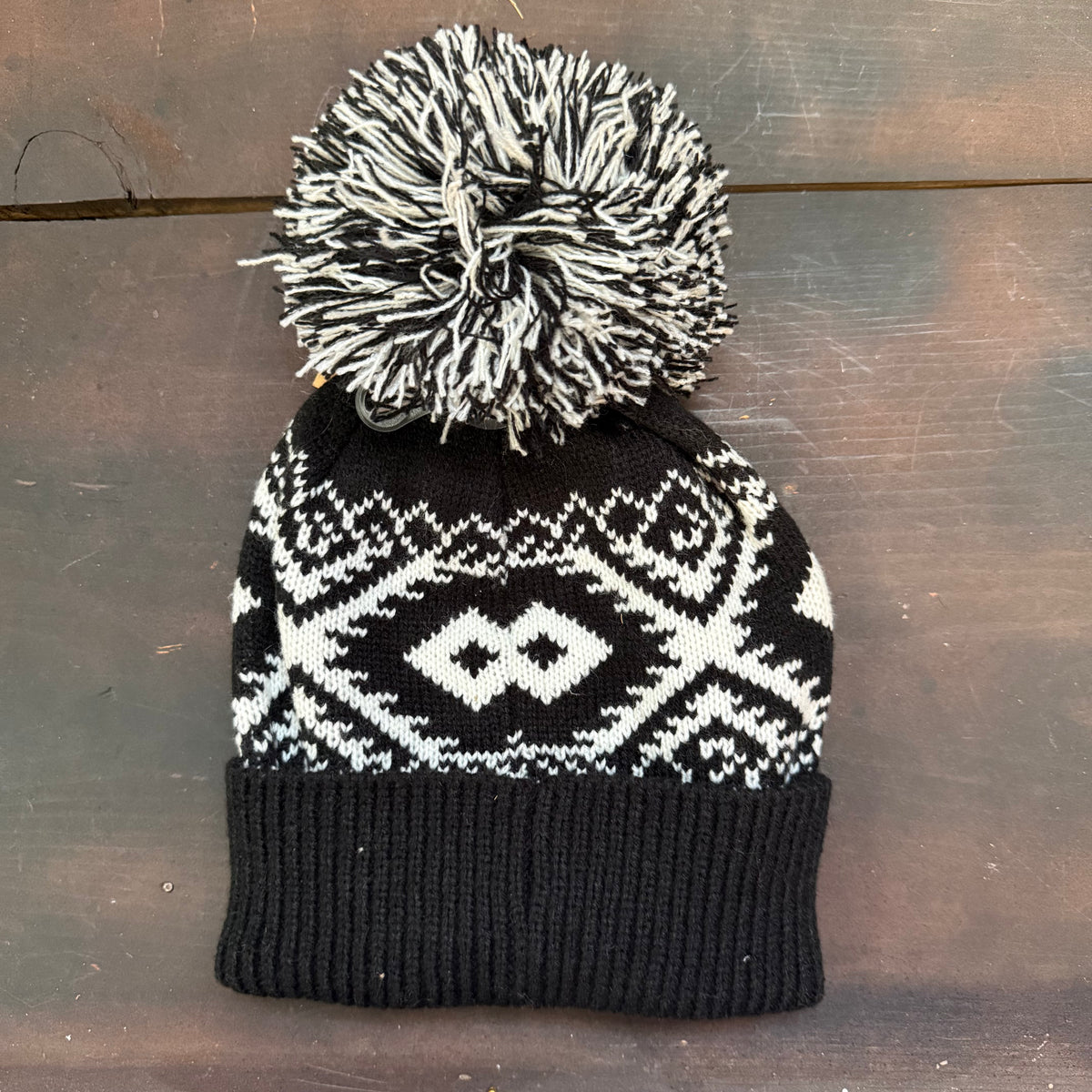 Black and white patterned knit beanie with a pom-pom on a wooden surface