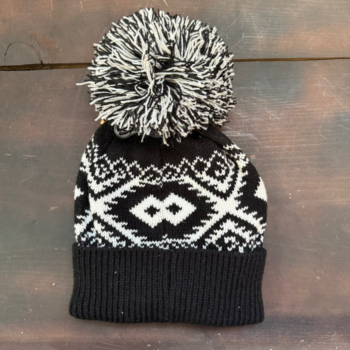 Black and white patterned knit beanie with a pom-pom on a wooden surface