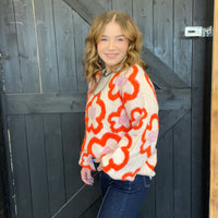 Woman wearing a colorful floral sweater standing in front of a wooden door.