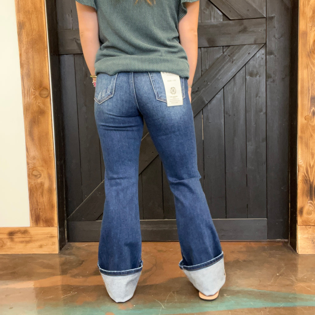 Person wearing blue jeans with white cuffs standing in front of a wooden door.