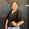 Woman wearing a black top and light blue jeans standing against a dark wooden wall.