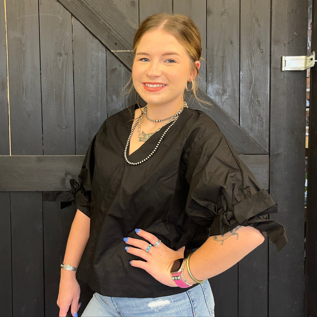 Woman wearing a black top and light blue jeans standing against a dark wooden wall.